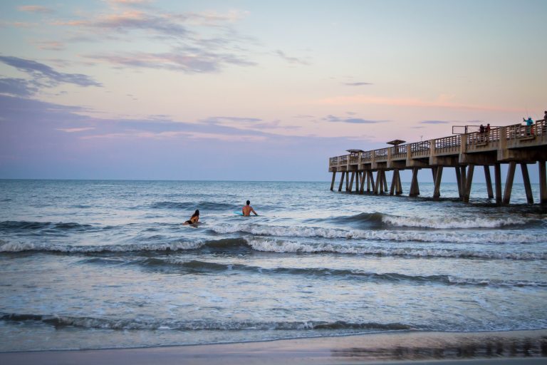 Sunset at the beach with pier and swimmers in the ocean.
