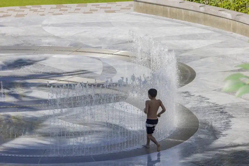 Child playing in a water fountain on a sunny day.